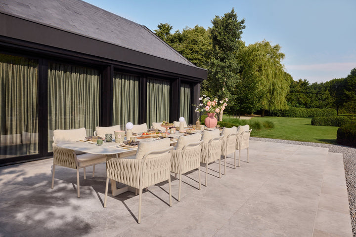 Gartenstühle mit hellem Geflecht um einen langen Gartentisch auf der Terrasse.