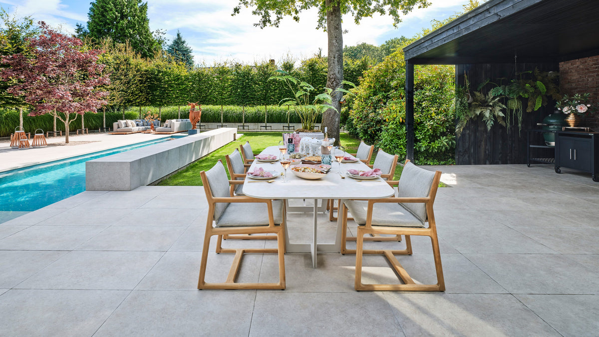 Gartentisch mit Holzstühlen und hellen Kissen auf einer Terrasse neben dem Pool.